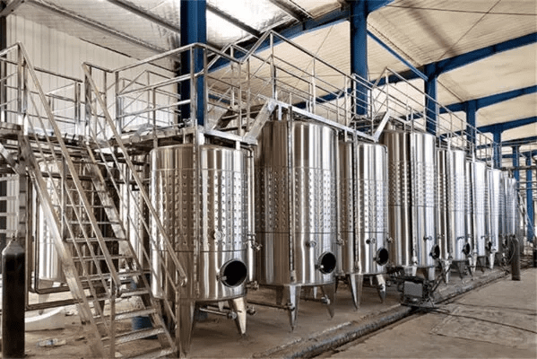 Zařízení pro vinařství 10000L fermentační tank na víno je velkokapacitní, průmyslové nádobí navržené pro efektivní fermentaci a skladování červeného vína, bílého vína a různých ovocných vín. Konstrukce z vysoce kvalitní nerezové oceli SUS304 nebo SUS316L, má robustní vnitřní skořepinu (typicky 3,0 mm) a vnější skořepinu (2,0 mm), v kombinaci s 80–100 mm polyuretanovou izolací, aby zajistila vynikající stabilitu teploty. Vybaveno pokročilými glycolovými chladicími obaly, umožňuje přesné ovládání teploty během celého procesu fermentace. Tank je navržen s kuželovým nebo plochým dnem pro flexibilní provoz a přichází kompletní s nezbytnými příslušenstvími, jako je horní uzávěr, CIP čisticí systém, ventil pro odběr vzorků, teplotní sonda, pojistný ventil a nastavitelné nohy. Jeho hygienický design, odolnost a uživatelsky přívětivá konfigurace z něj činí ideální řešení pro komerční vinařství, která hledají spolehlivé a vysoce výkonné fermentační zařízení.